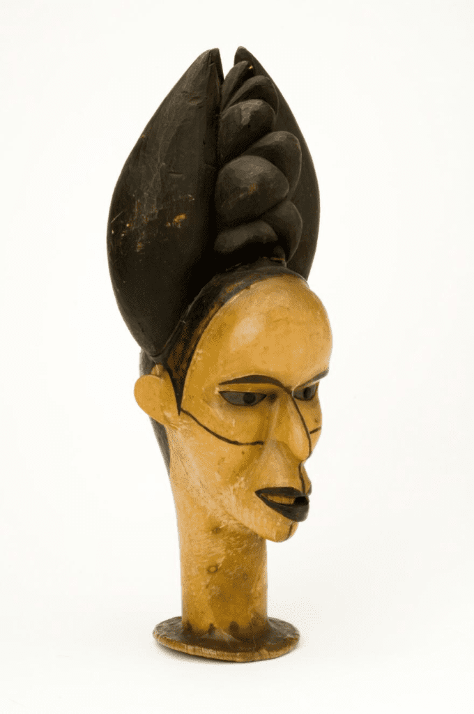 A female head with elaborate coiffure from the Ibo People, West Africa. The wooden headdress is covered with skin and has eyes of zinc. Wellcome Collection.