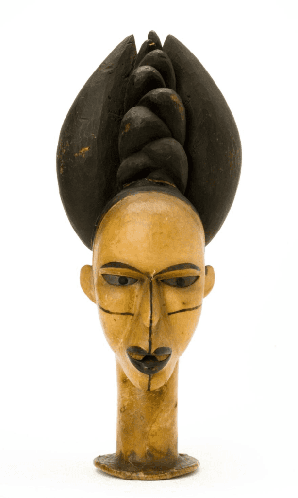 A female head with elaborate coiffure from the Ibo People, West Africa. The wooden headdress is covered with skin and has eyes of zinc. Wellcome Collection.